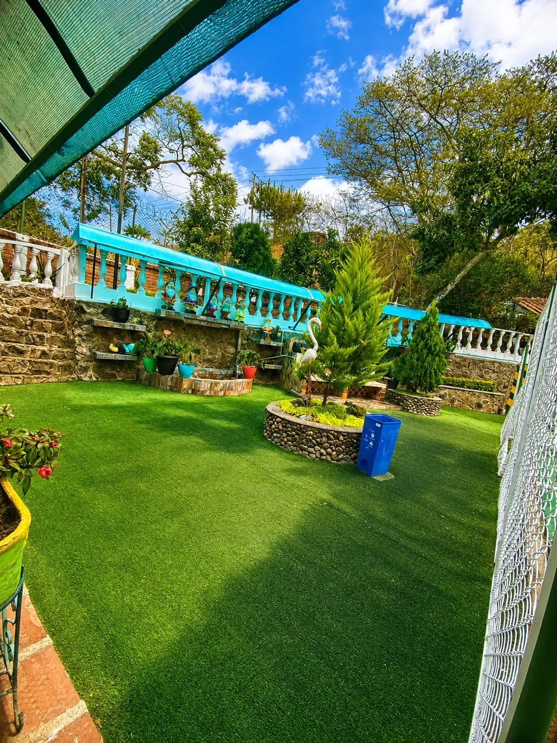 Zona verde con grama sintética, jardines y pérgola azul
